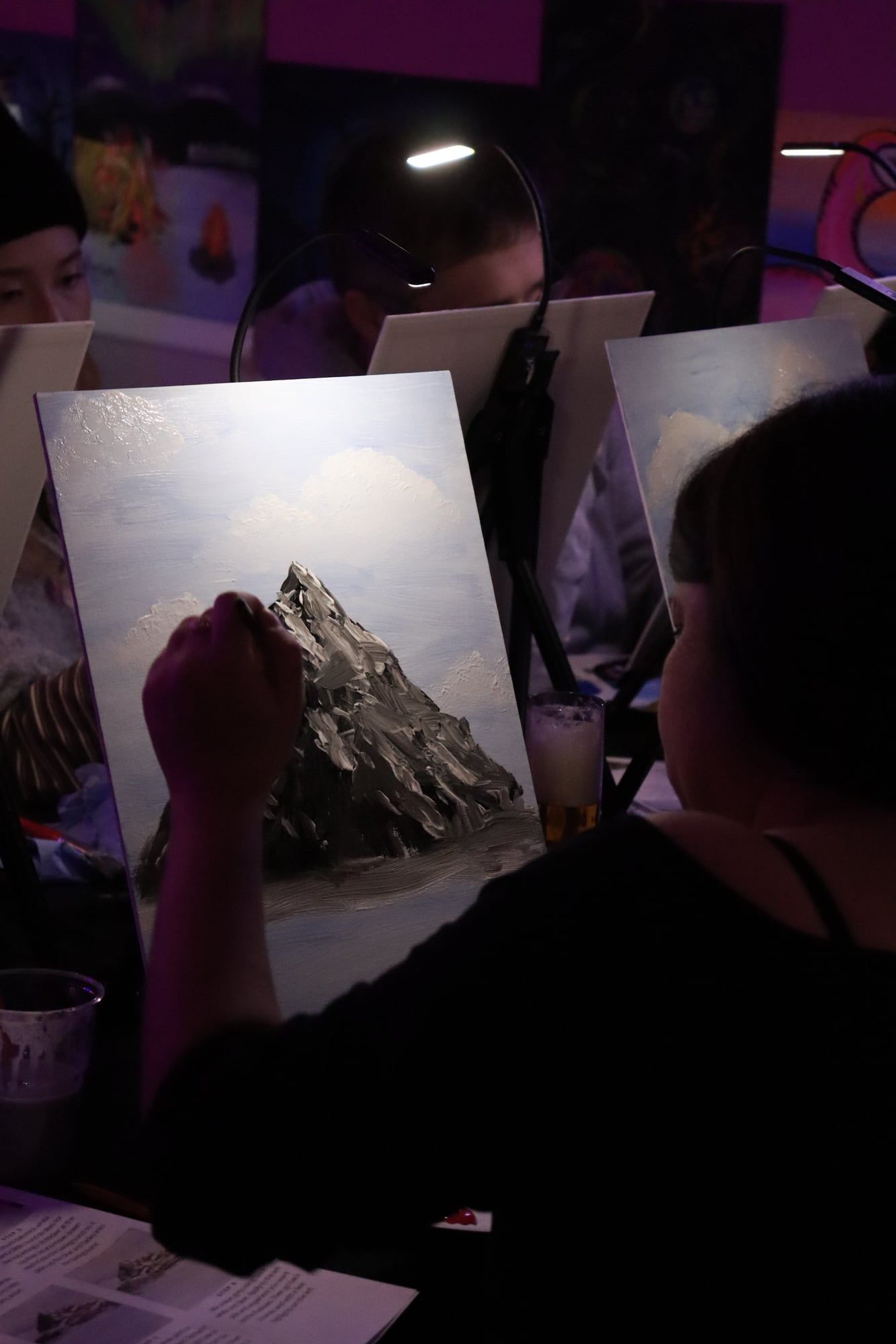 Guest painting a detailed mountain landscape on a canvas during an art class