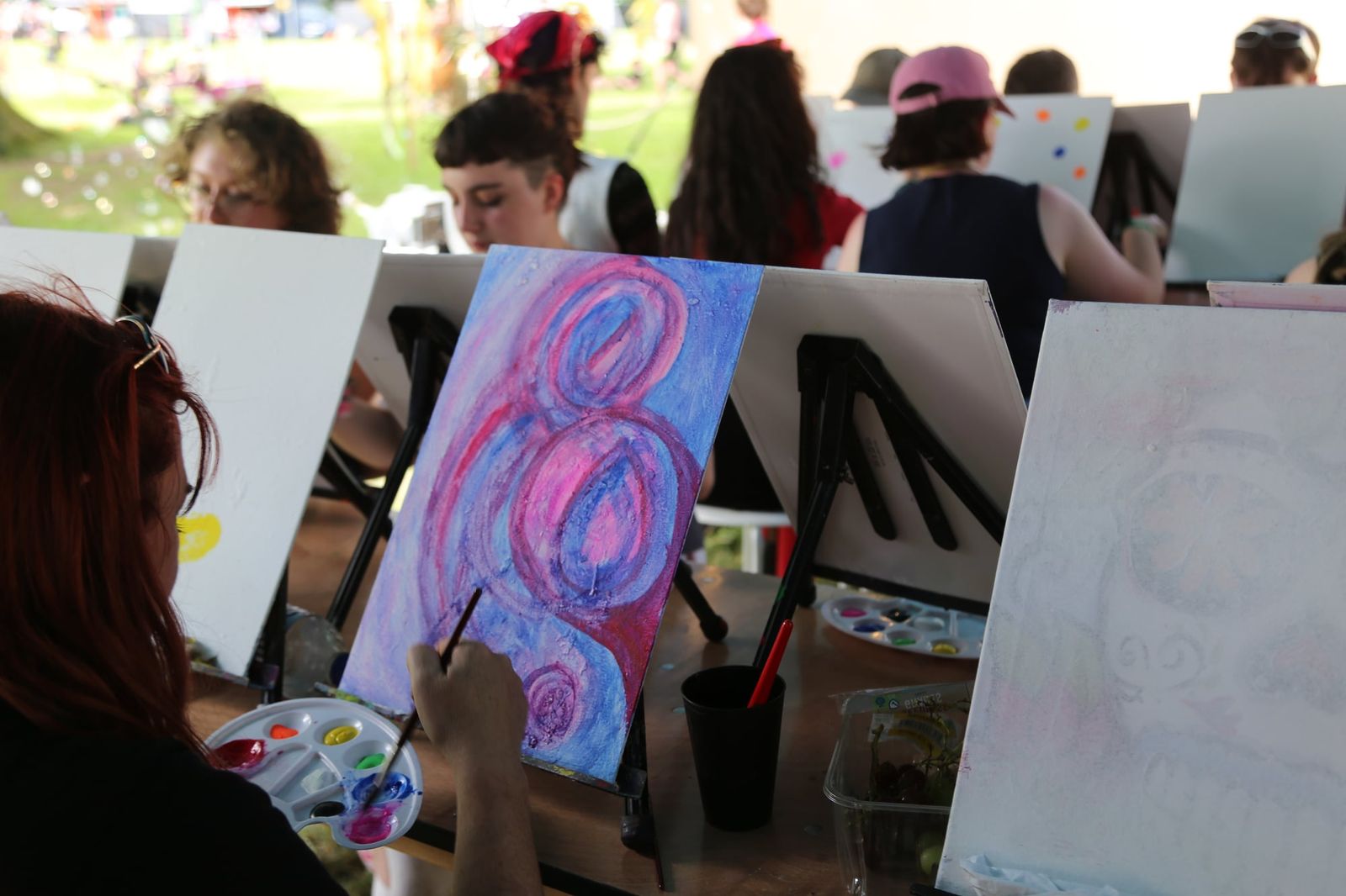 Guest painting pink and purple abstract swirls during an outdoor art workshop