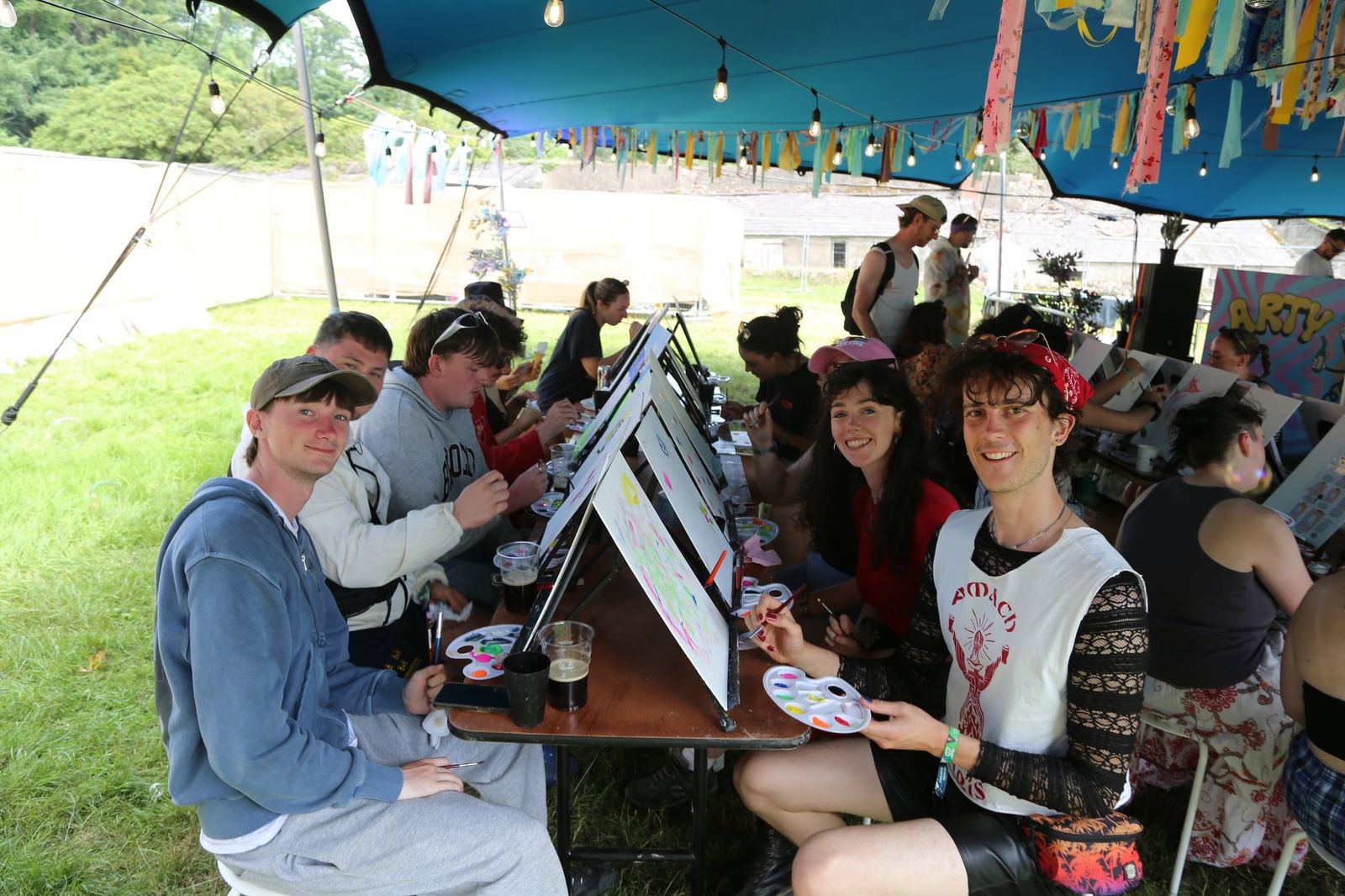 Group of friends sitting at a long table during an outdoor paint and sip class