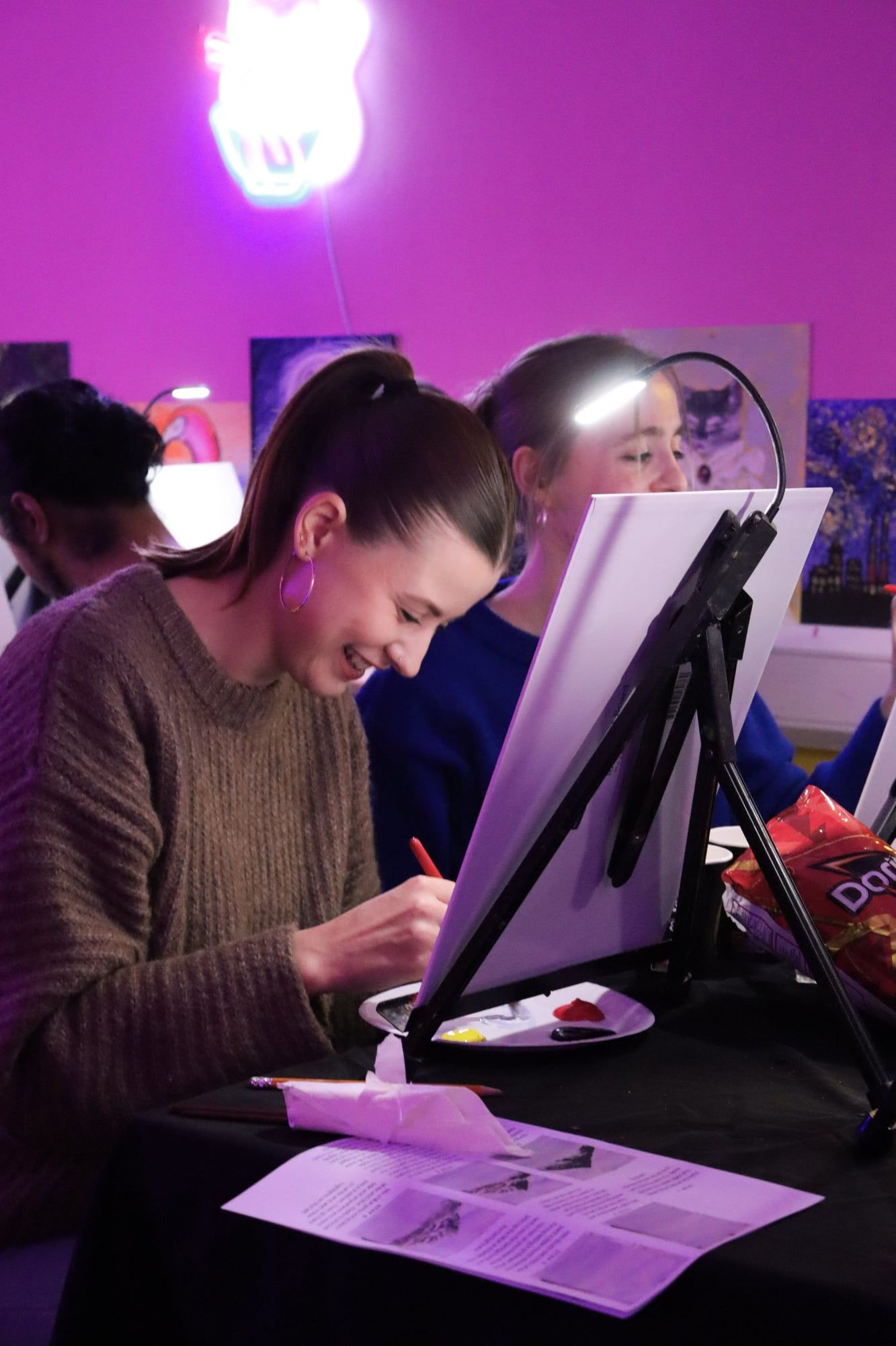Smiling guest painting a canvas under purple lighting at a paint and sip workshop