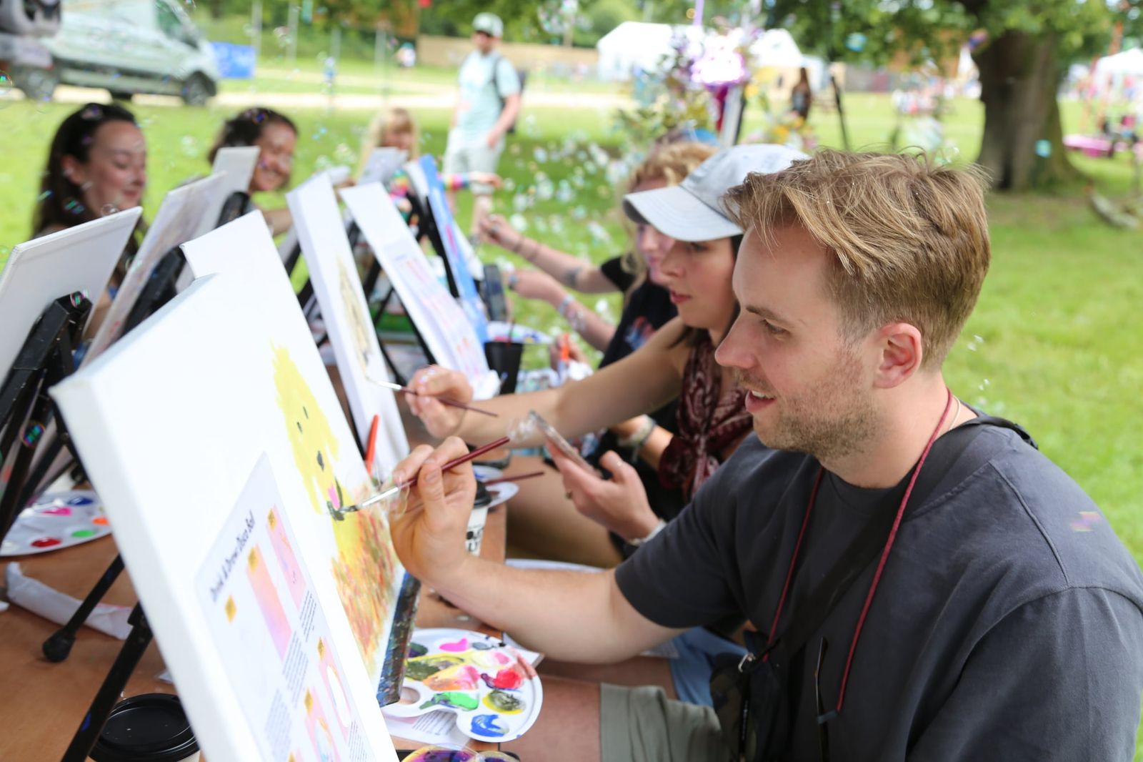 Man smiling while painting at a shared table during an outdoor paint and sip event