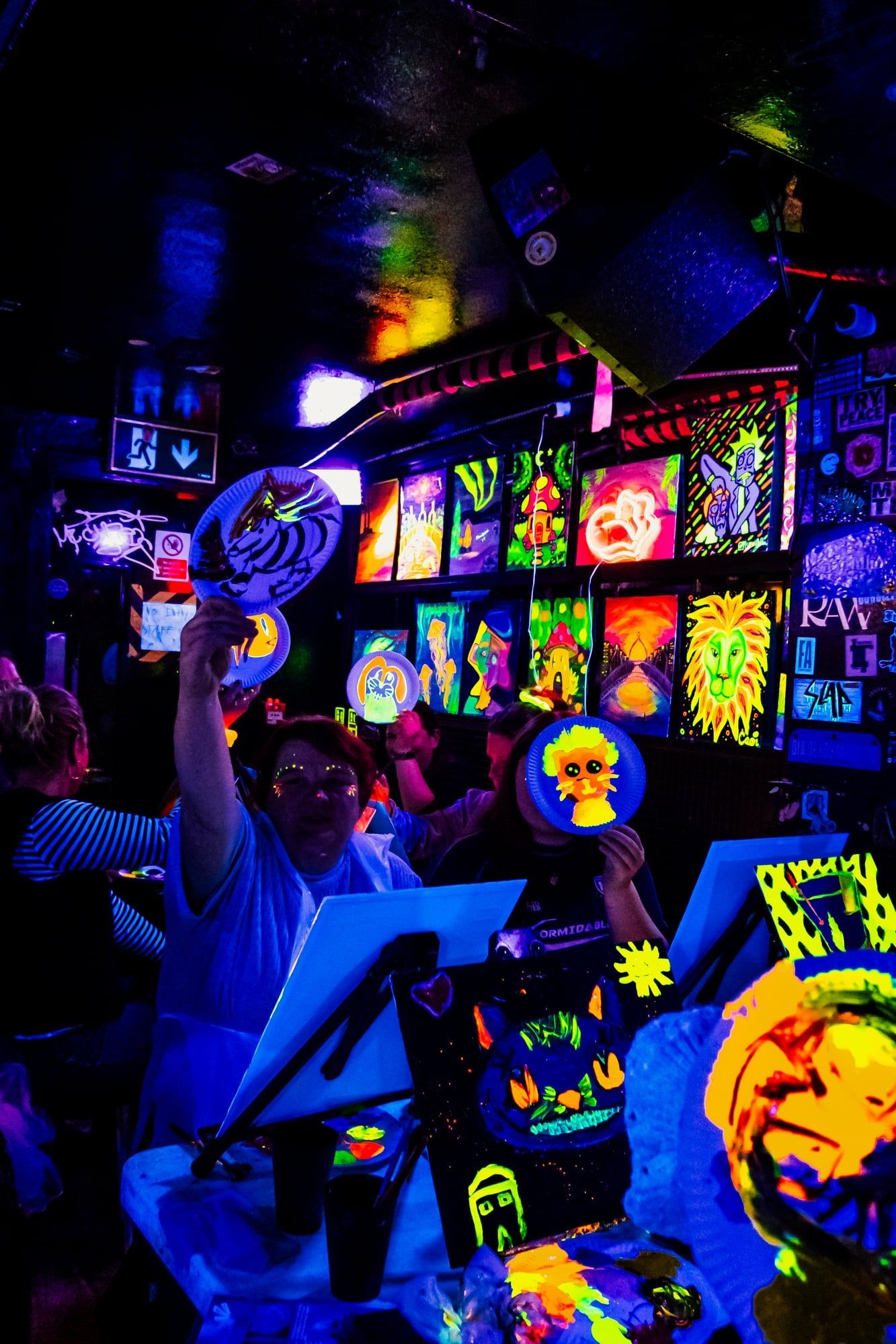 Guests holding up their glowing neon plate paintings at a lively workshop