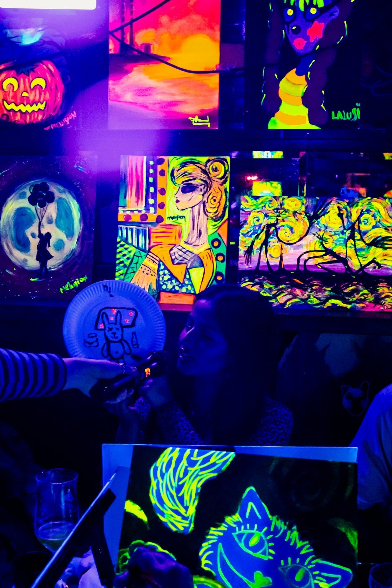 Guest working on a small neon plate painting with glowing artworks in the background