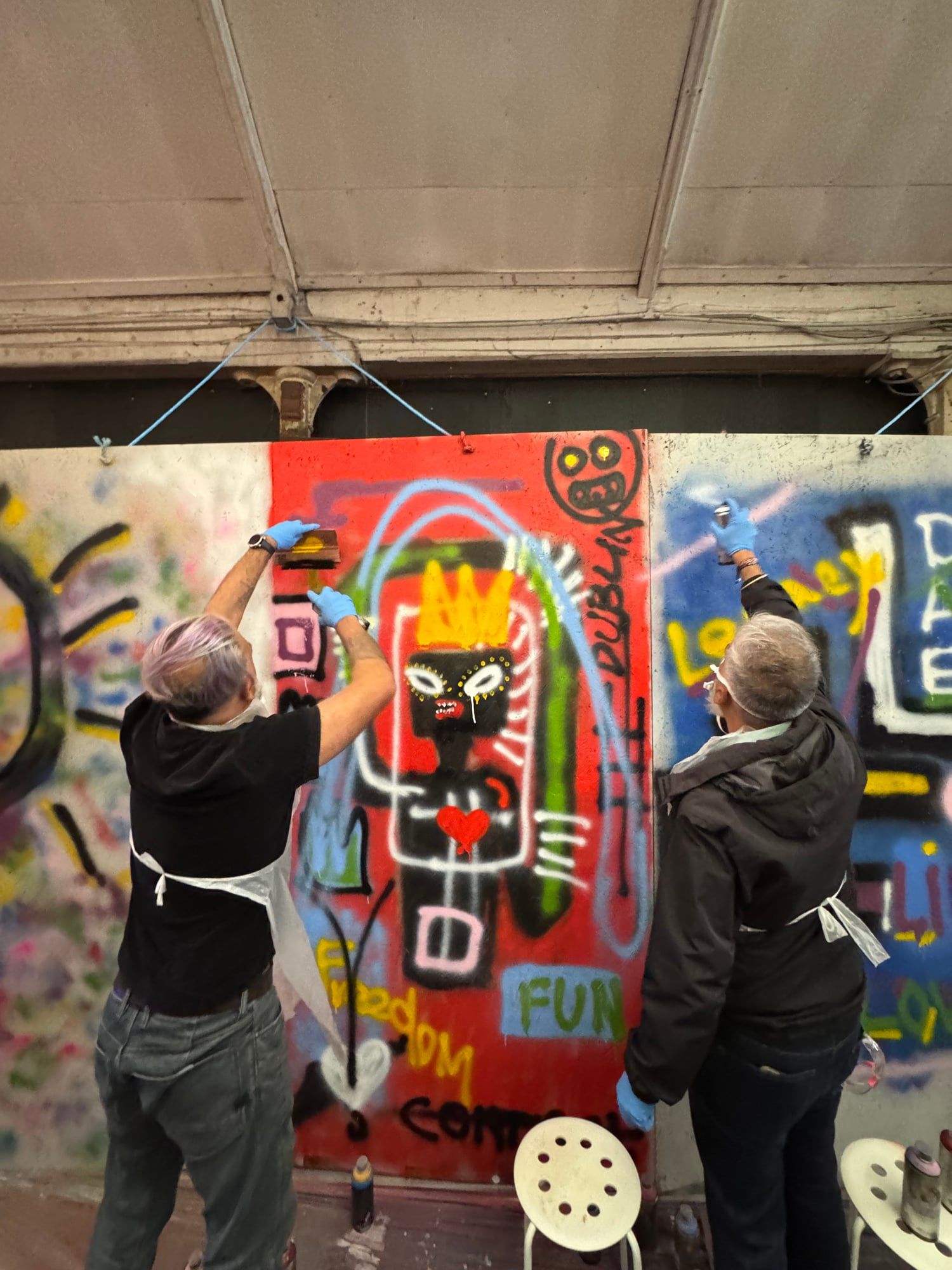 Two guests painting a vibrant figure on a wall during a graffiti workshop