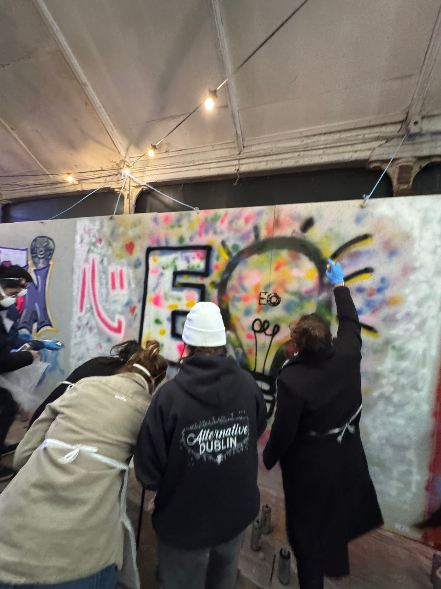 Three guests spray painting colorful letters on a board at a graffiti class