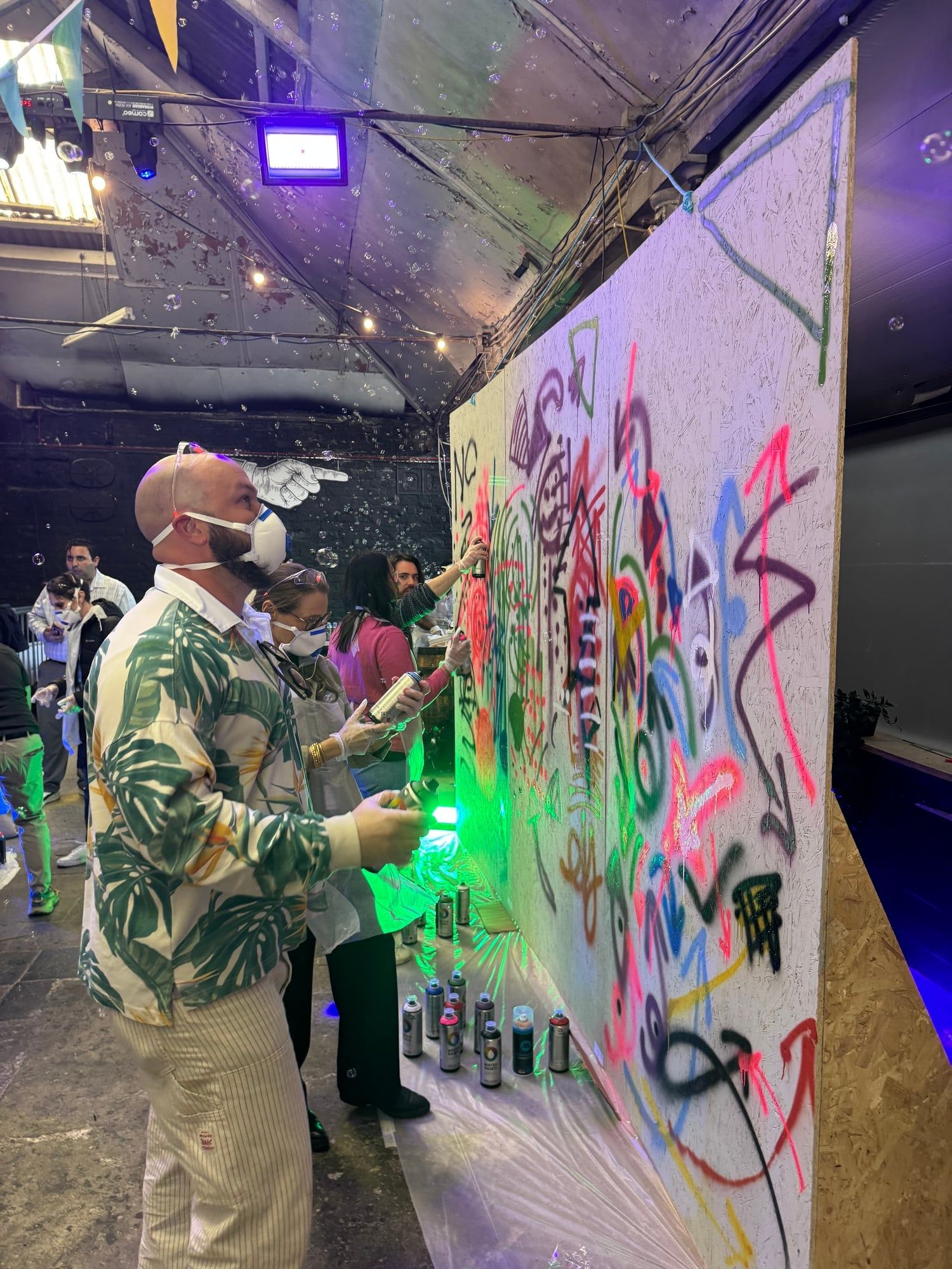 Guest in a patterned shirt spraying a colorful wall at an indoor graffiti workshop