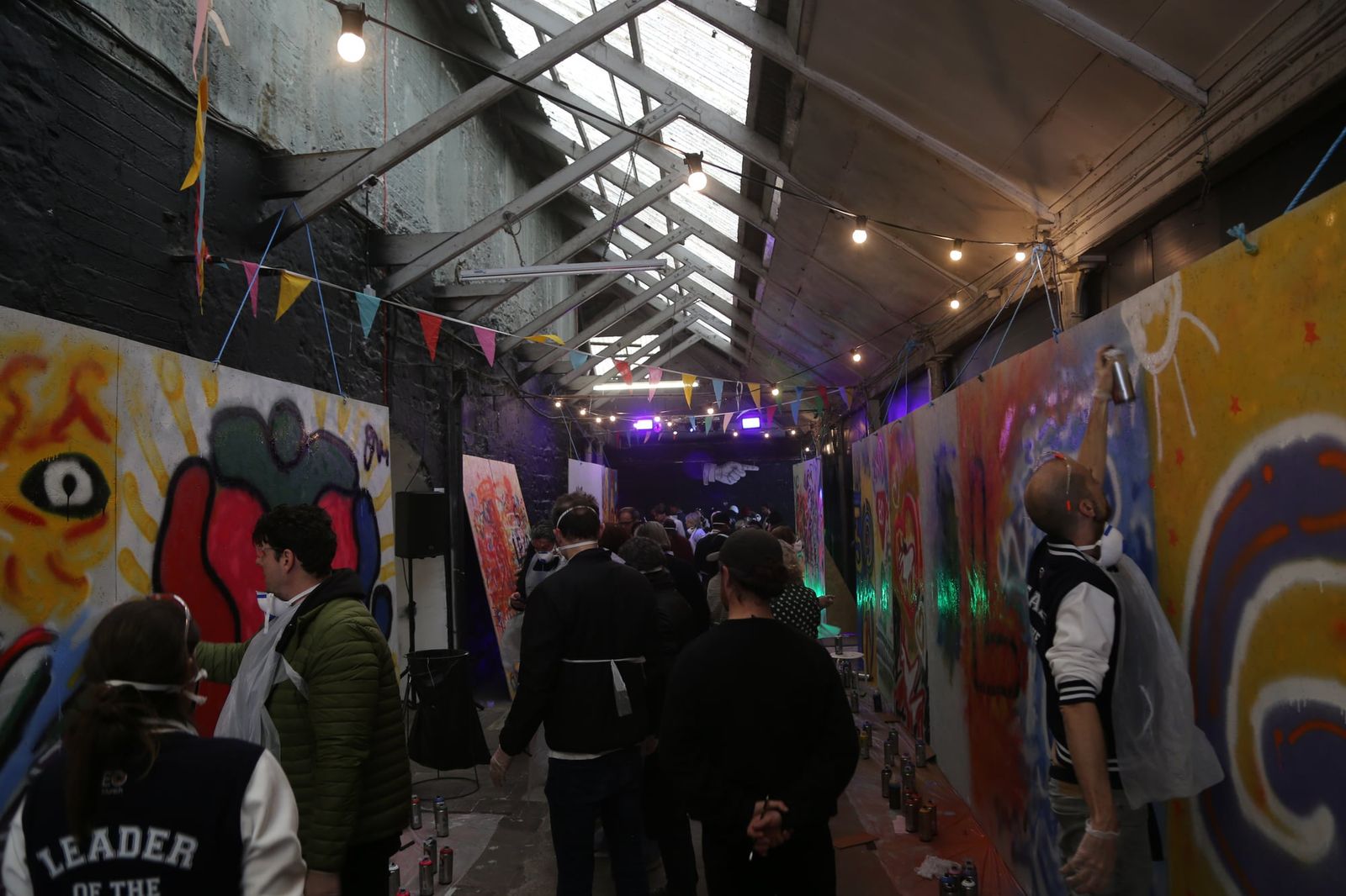 Long view of guests painting along a large indoor wall at a graffiti workshop