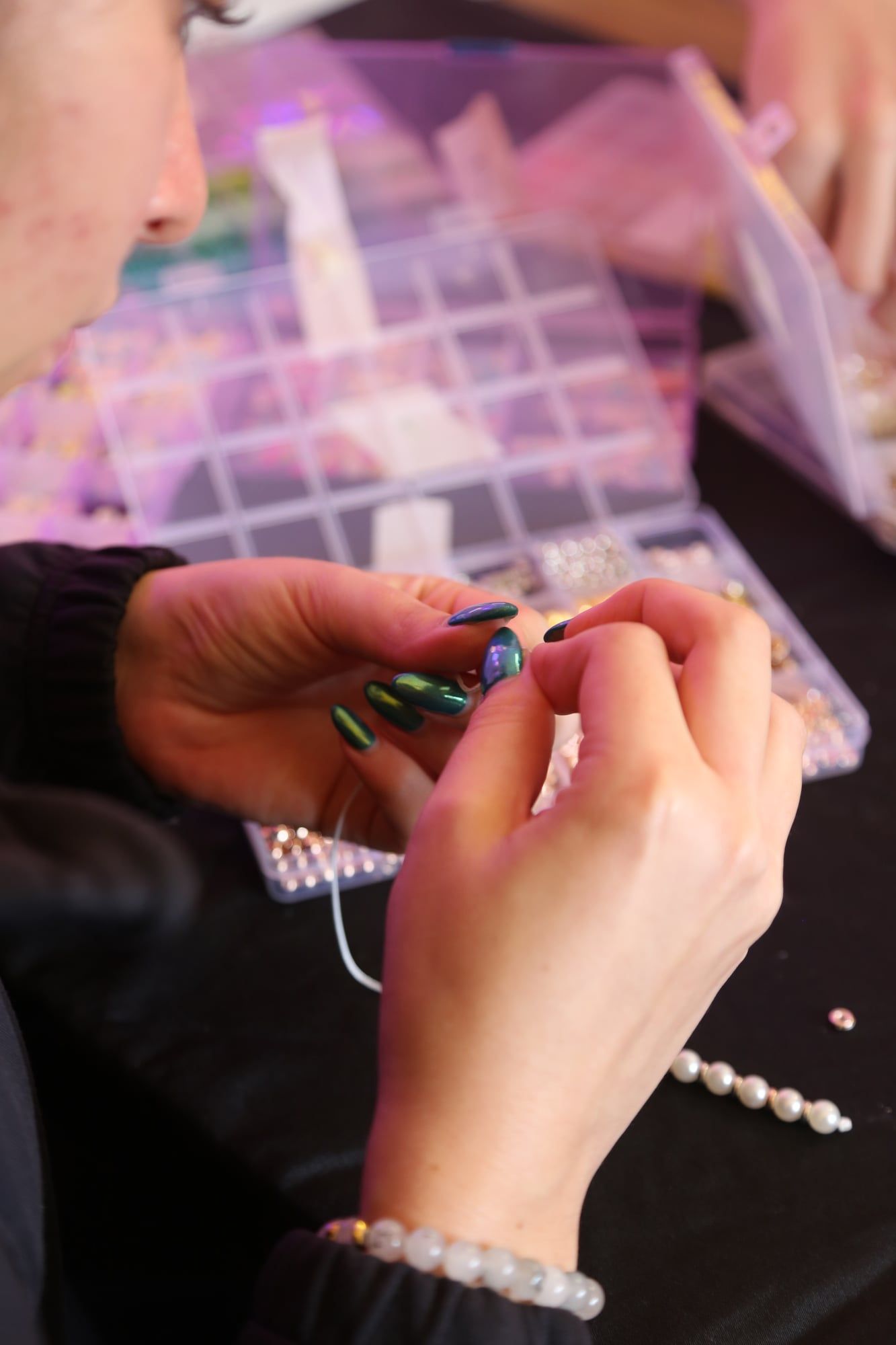 Close-up of hands attaching a clasp to a beaded necklace at a workshop