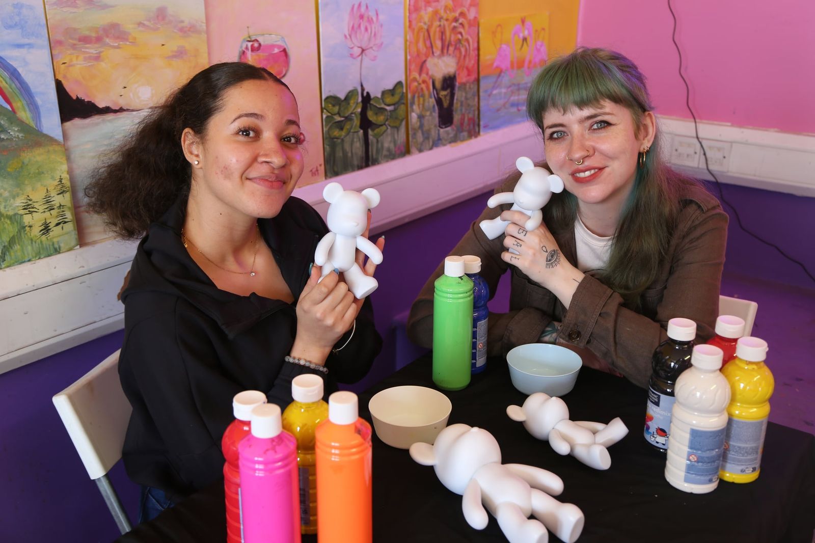 Two women holding blank bear figurines ready to paint at a workshop