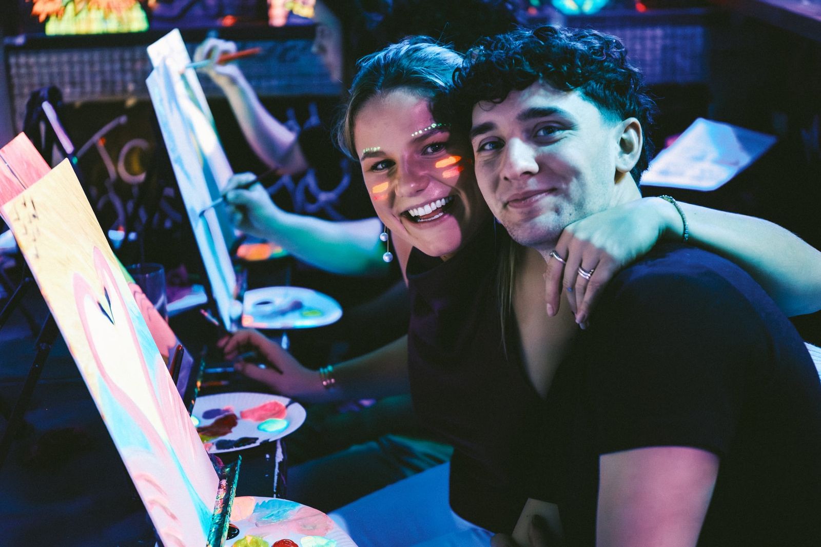 Two guests smiling while painting together at a neon glow in the dark workshop