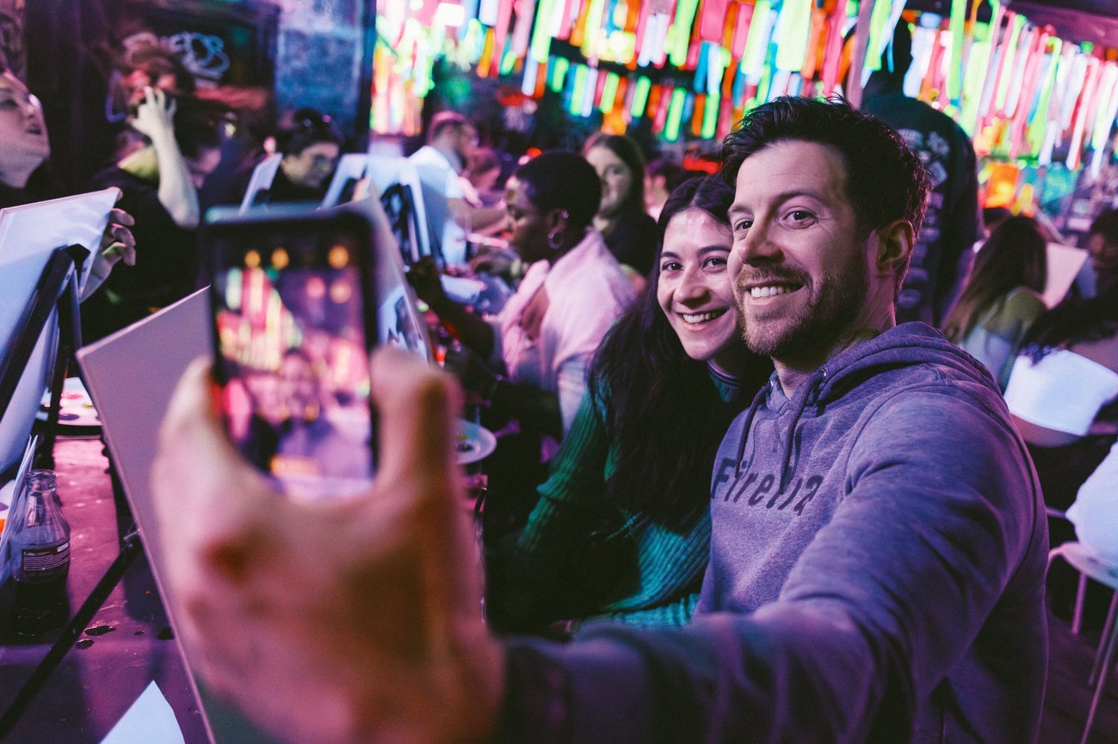 Guest taking a selfie with a friend while painting at a neon workshop