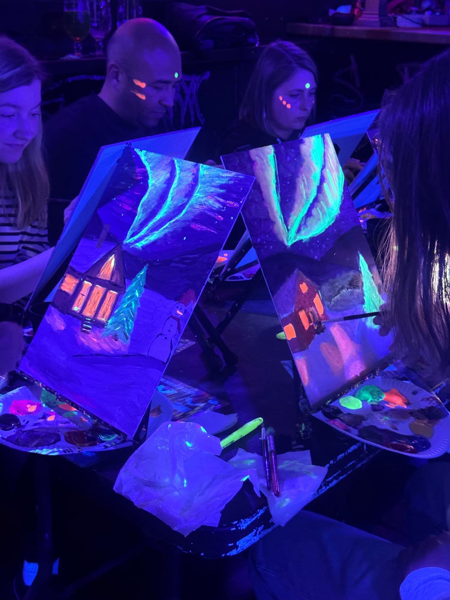 Close-up of a glowing canvas painting of a snowy cabin at a neon workshop