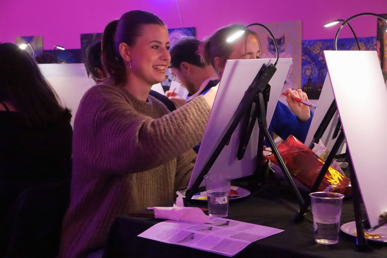 Woman laughing happily while painting her canvas at an indoor paint and sip class