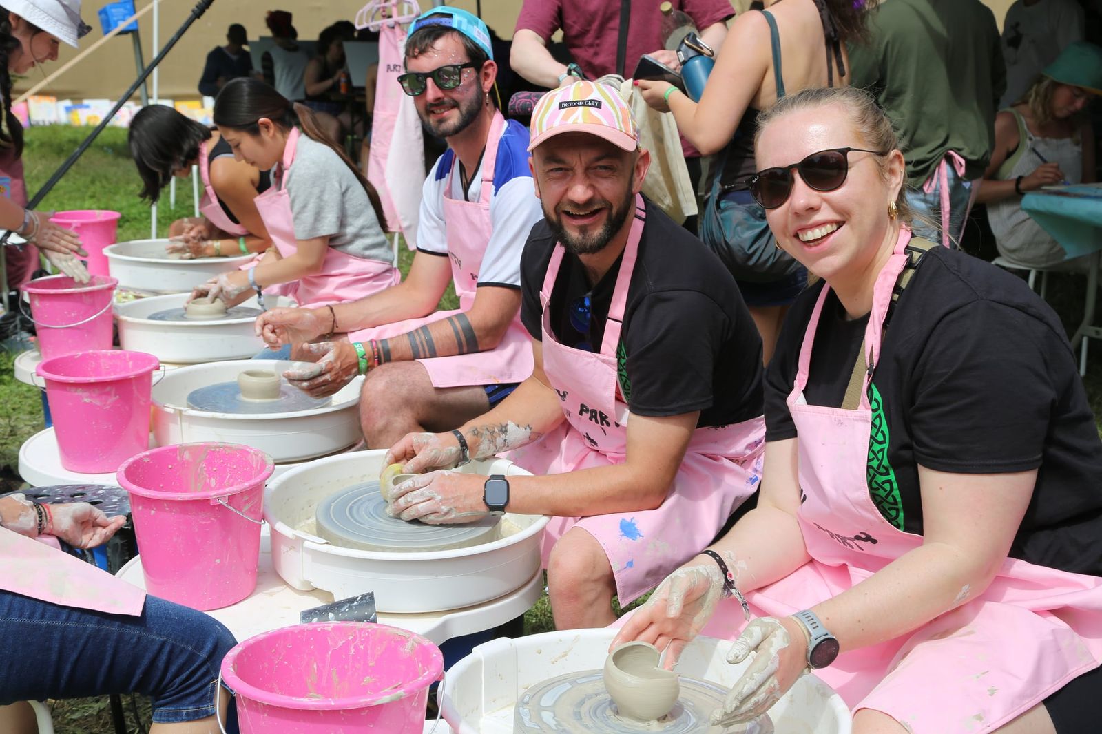 Group of guests smiling at outdoor pottery wheels during a group event