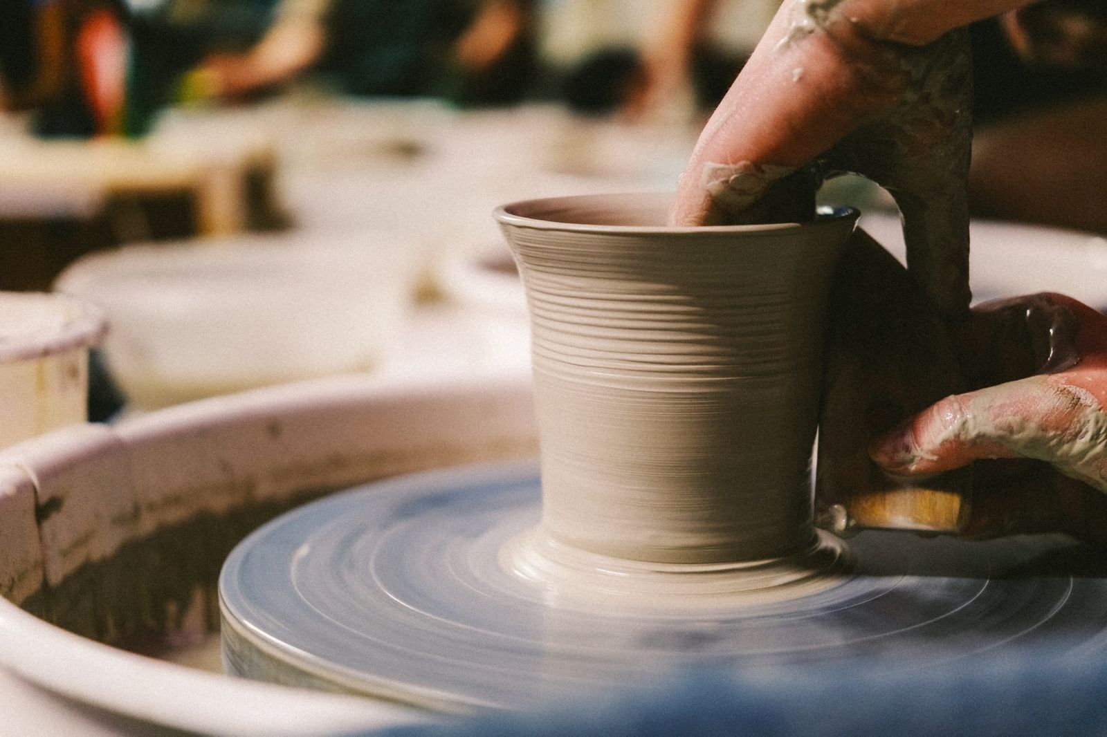 Close-up of hands pulling up the walls of a clay vessel on a pottery wheel