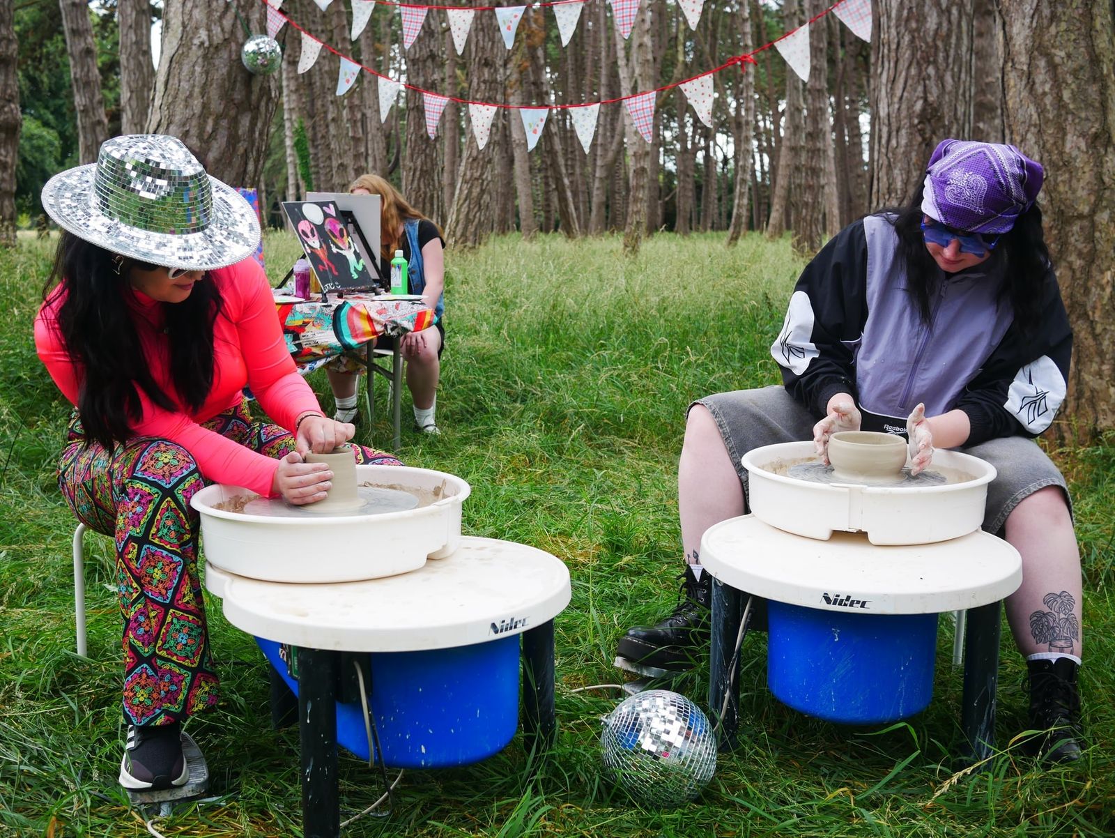 Two guests wearing sparkly hats working at outdoor pottery wheels