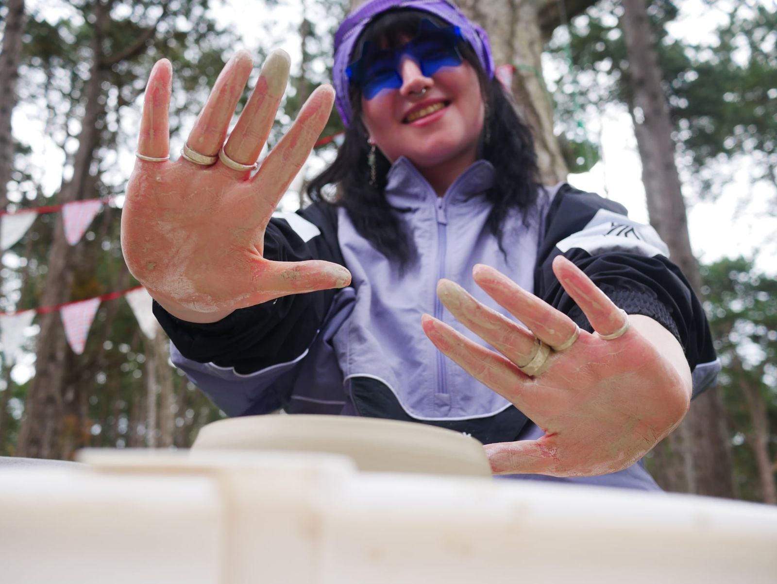 Smiling guest showing her clay-covered hands at an outdoor pottery wheel class