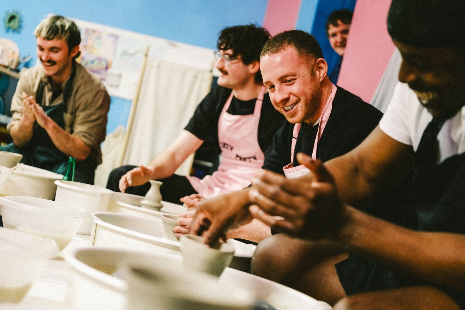 Group of men smiling and working at pottery wheels during a group class