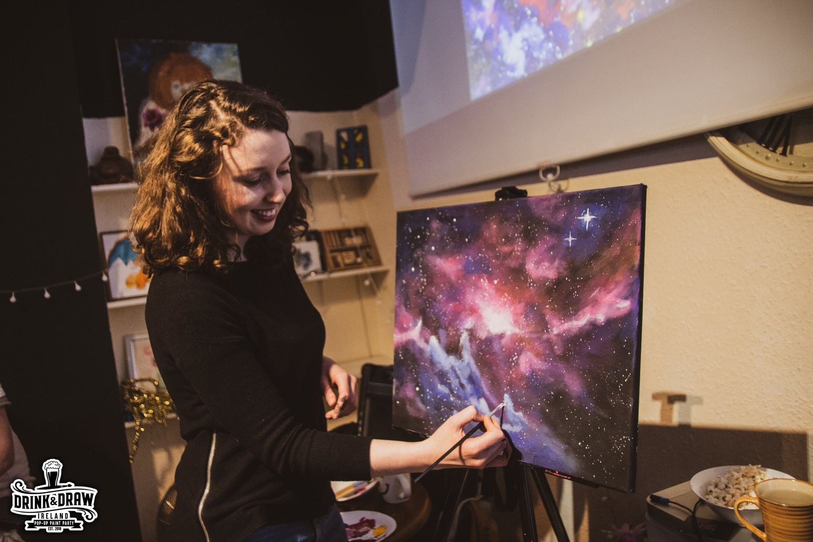 Guest smiling while painting a colourful galaxy canvas at a paint and sip event