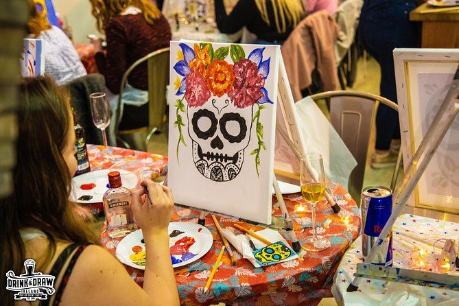 Guest painting a decorated skull canvas at a paint and sip table with drinks and art supplies